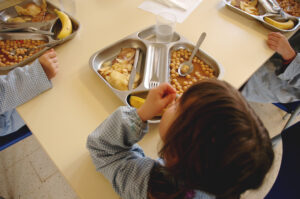 A child with their stainless steel lunch tray sitting at a cafeteria table