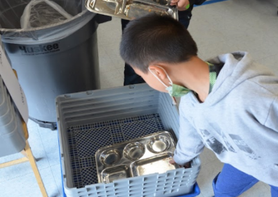 A student depositing an empty metal tray in a bin